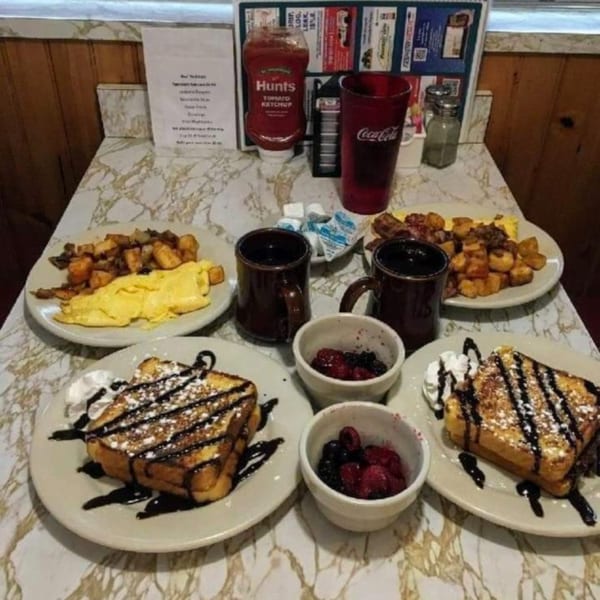 Diner breakfast spread with French toast, scrambled eggs, home fries, and berries on a marble table.