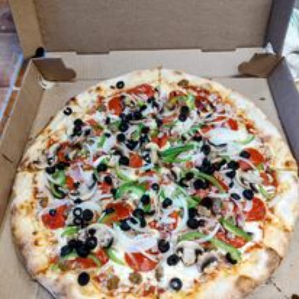 A large, fully loaded pizza with pepperoni, olives, peppers, onions, and mushrooms in a cardboard box.