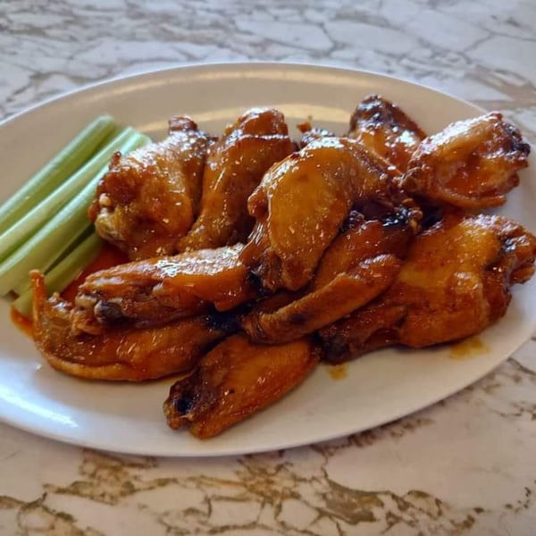 A plate of Gus' Red Hots diner-style chicken wings, coated in sauce, with celery sticks.
