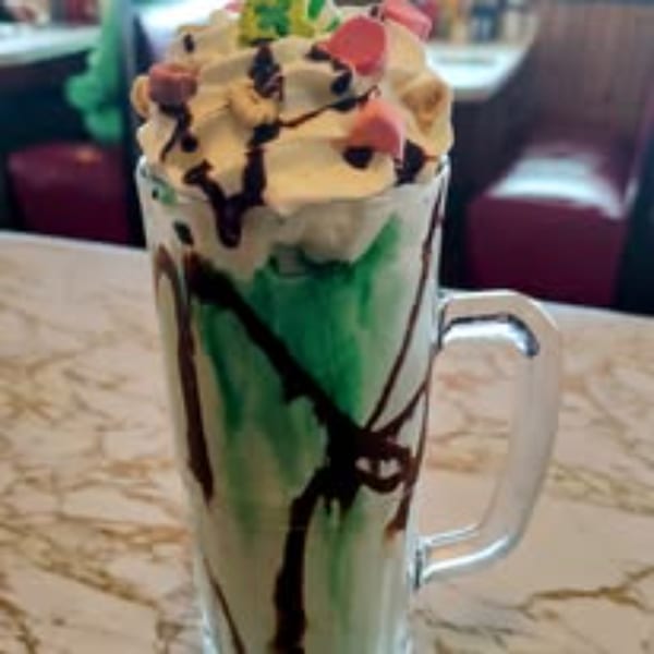 Green milkshake with whipped cream, chocolate drizzle, and colorful marshmallows at Gus' Red Hots.