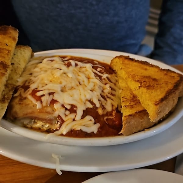 A bowl of lasagna with melted cheese and red sauce, served with two pieces of garlic bread.