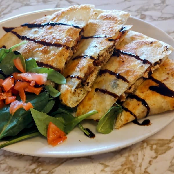 Quesadilla slices drizzled with balsamic glaze, served with a side of spinach and diced tomatoes.