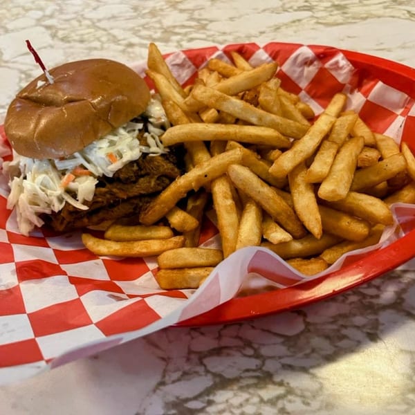 Pulled pork sandwich with coleslaw and a side of golden fries in a red basket.
