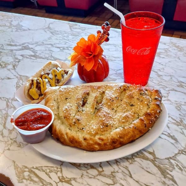 A calzone, hot dog, red soda, and marinara on a marble table at Gus' Red Hots diner.