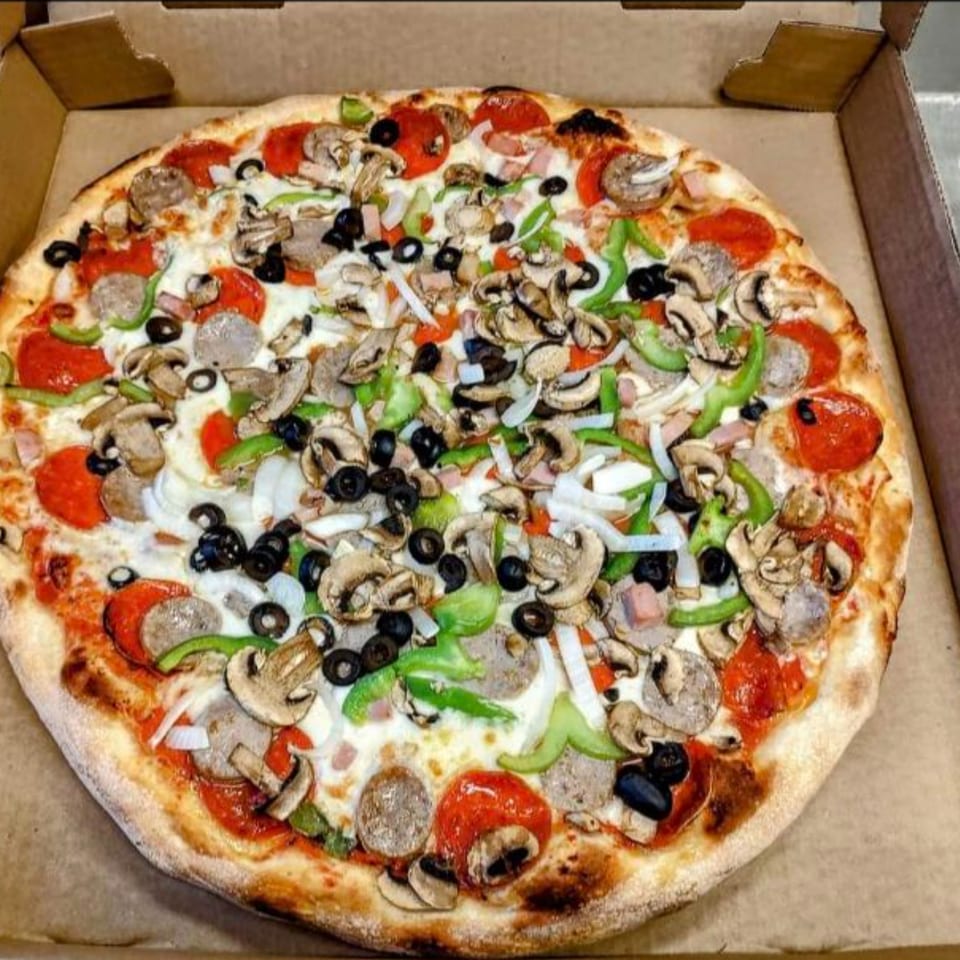 A Gus' Red Hots pizza in a box, topped with pepperoni, sausage, mushrooms, olives, and peppers.