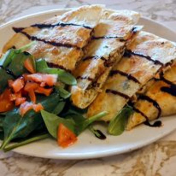 A plate of golden-brown quesadillas drizzled with balsamic glaze, served with a side salad of spinach and diced tomatoes.