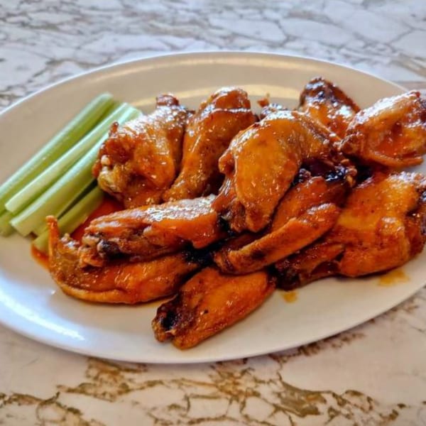 A white plate of Gus' Red Hots buffalo wings with celery sticks on a marble table.
